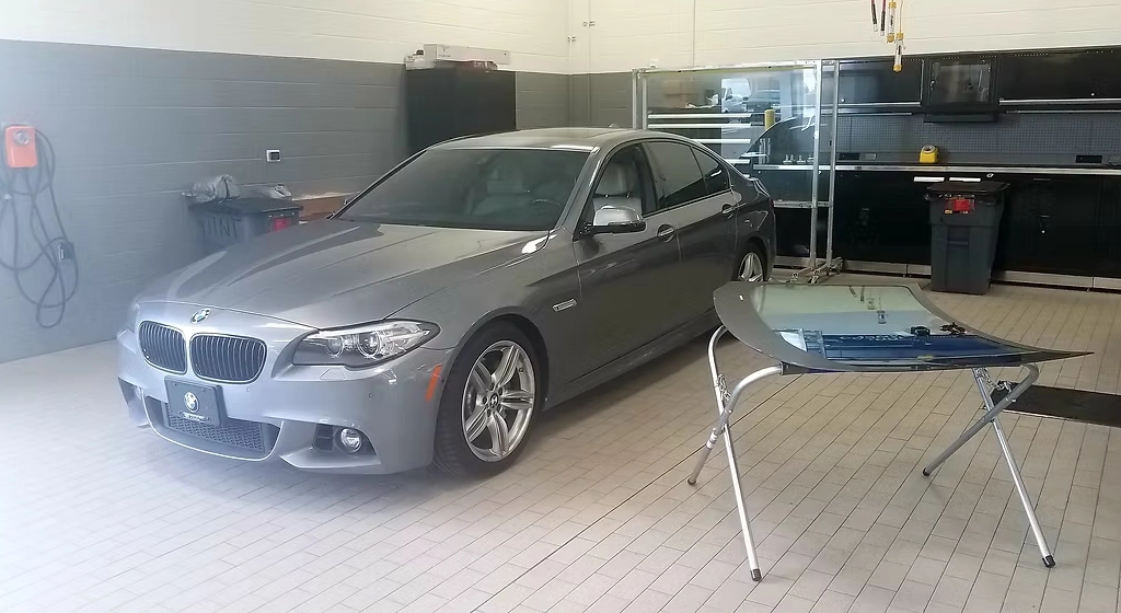 New windshield laid out on a stand next to a BMW sedan in the shop bay